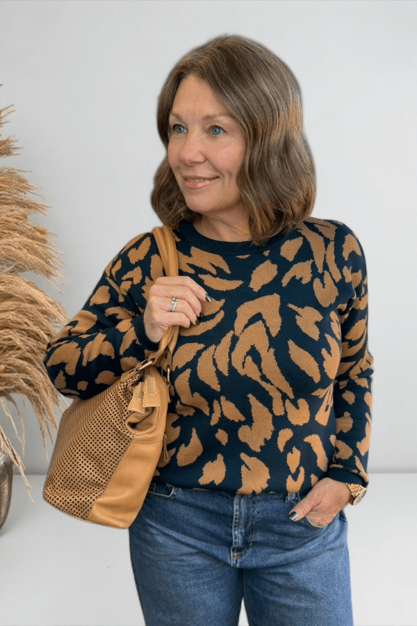 Woman wearing a patterned sweater and holding a brown bag against a white background