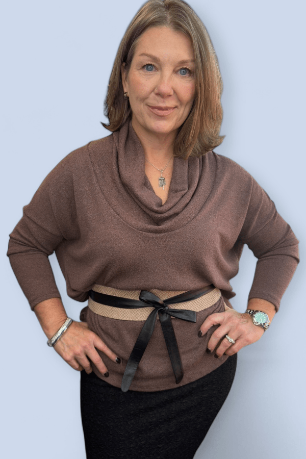 Woman wearing a brown cowl-neck sweater with a black belt against a light blue background