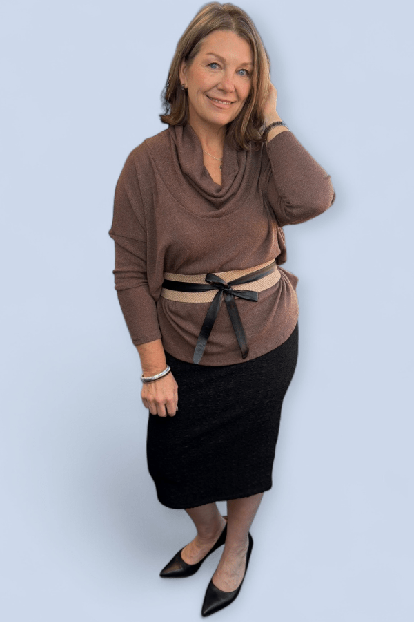 Woman wearing a brown cowl-neck sweater and black skirt against a light blue background