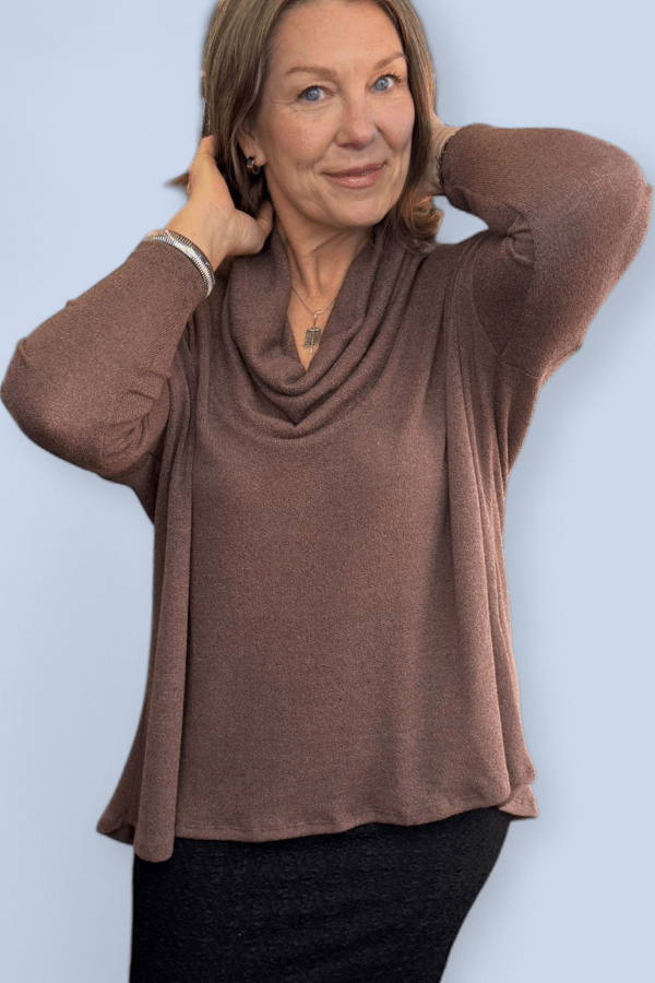 Woman wearing a brown cowl-neck sweater against a light blue background