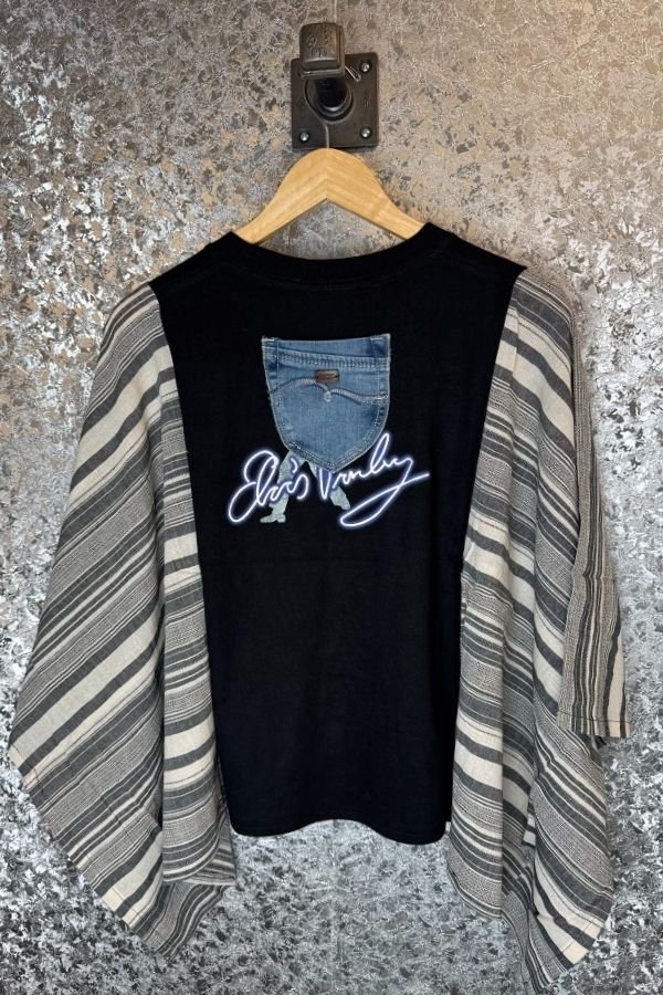 Black sleeveless top with denim pocket design and 'Elvis Presley' logo on a striped garment, hanging against a textured wall.