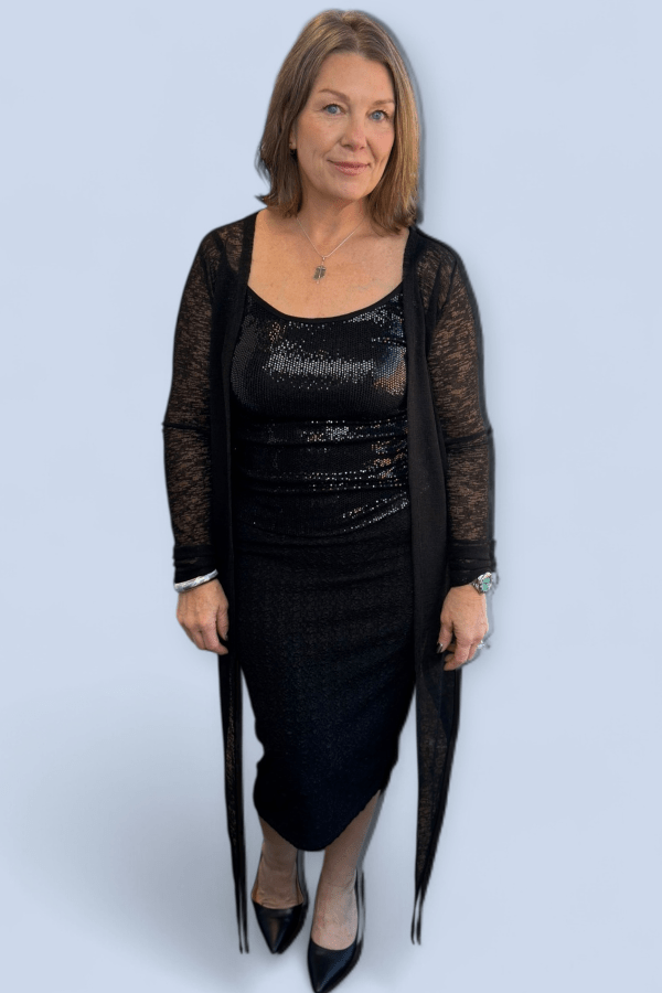 Woman wearing a black sequin top with a sheer black cardigan on a light blue background