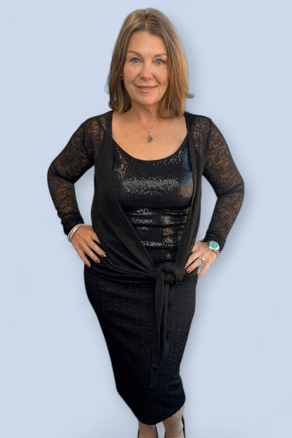 Woman wearing a black dress with a matching cardigan against a light blue background