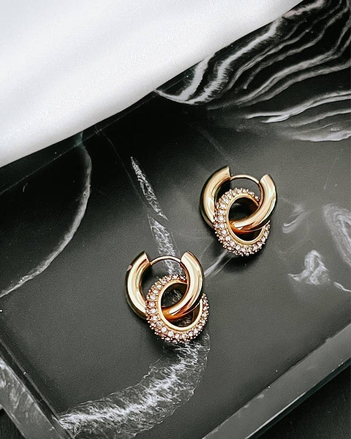 Pair of gold hoop earrings with interlocking design on a black marble surface