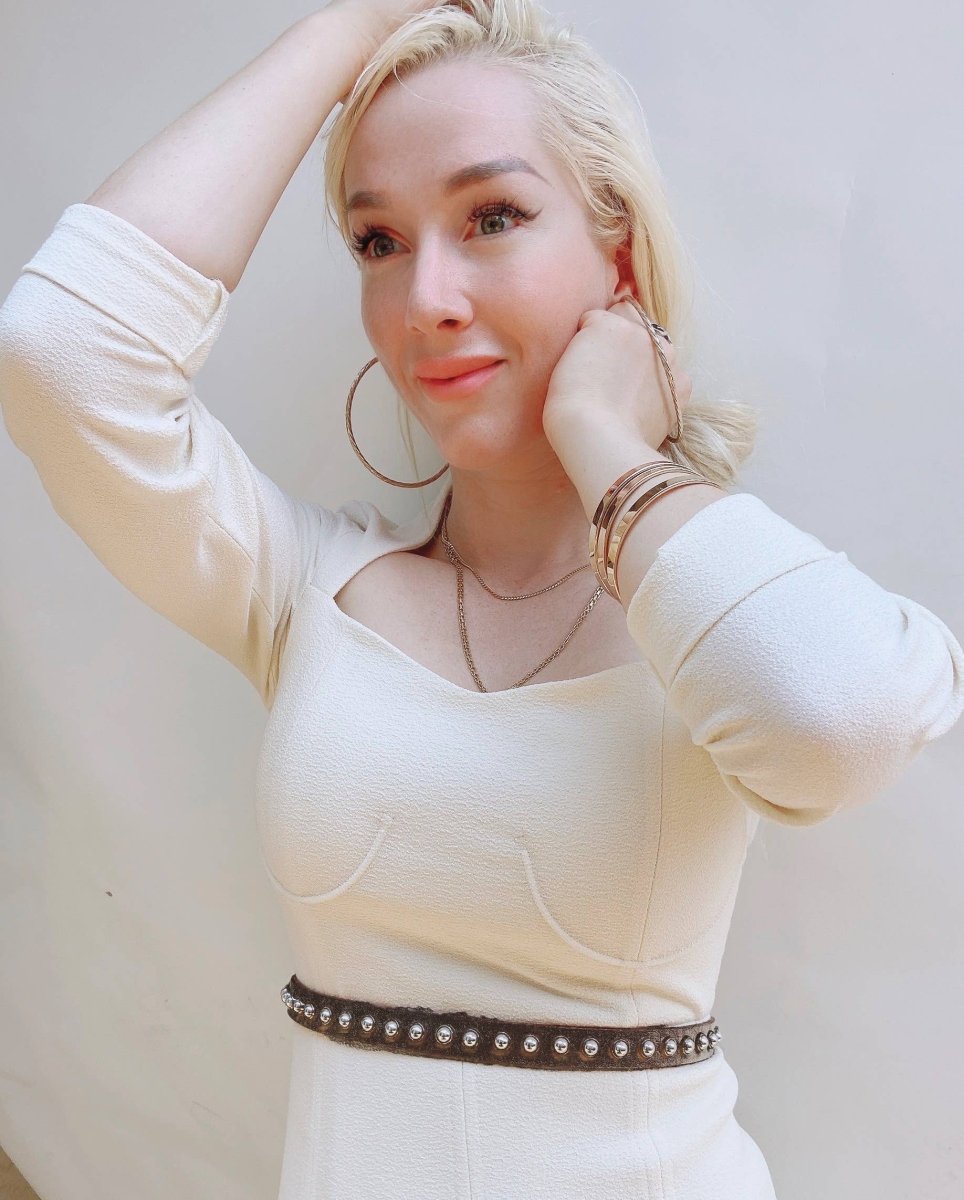Woman wearing a white long-sleeve top with a studded belt against a plain background