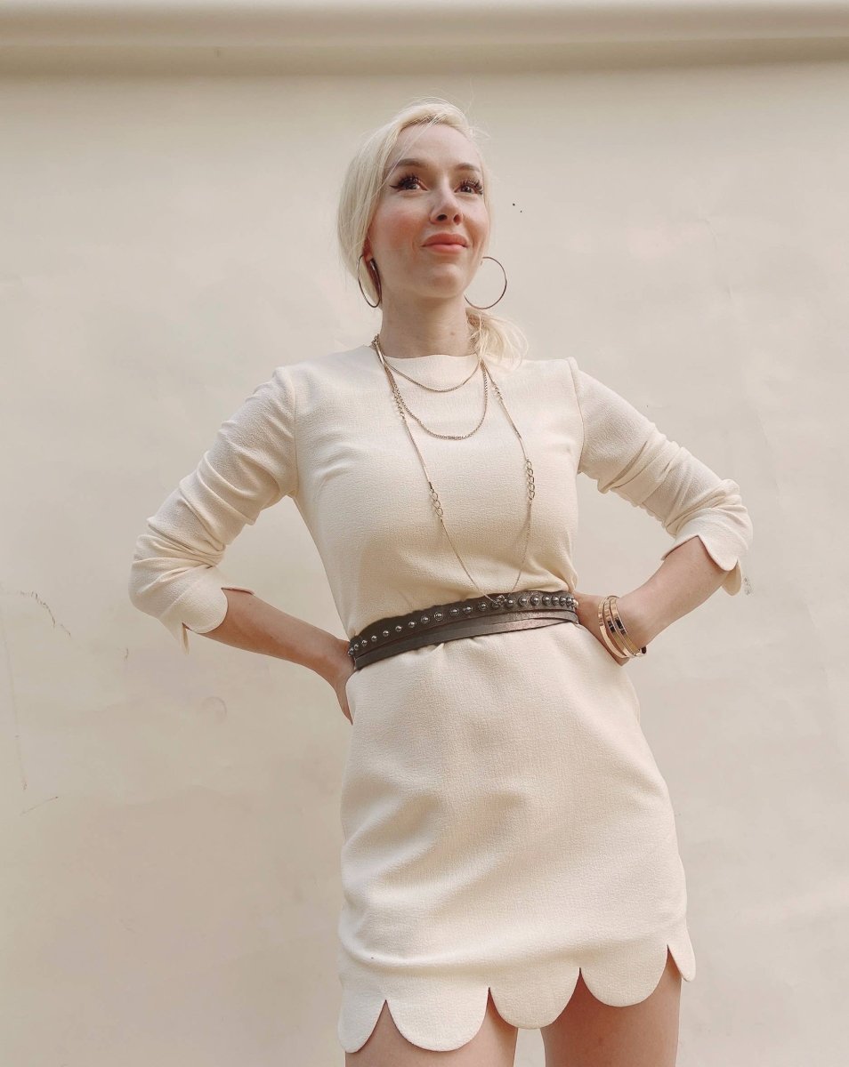 Woman wearing a white dress with a scalloped hem against a plain background