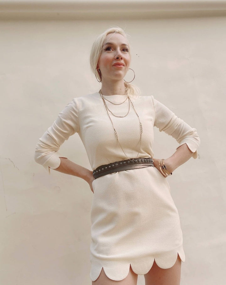 Woman wearing a white dress with a scalloped hem against a plain background
