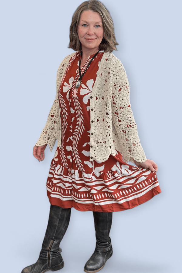 Woman wearing a red and white patterned dress with a beige lace cardigan on a light blue background