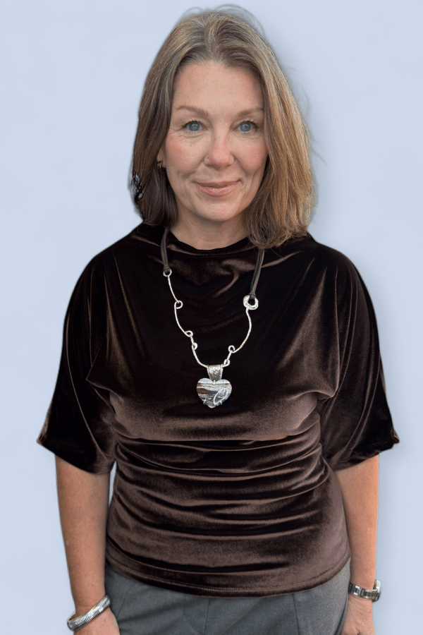 Woman wearing a brown velvet top with a necklace against a light blue background