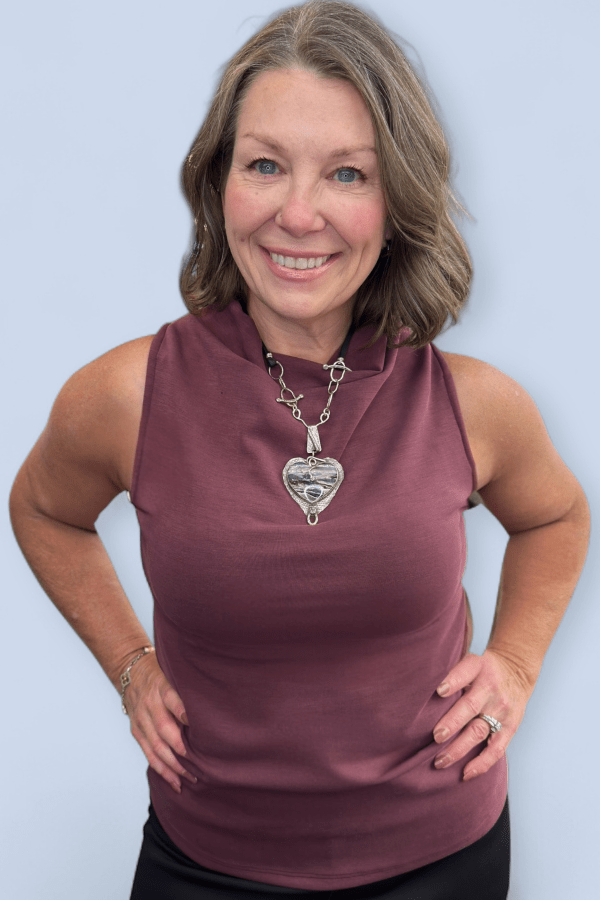 Woman wearing a maroon sleeveless top with a necklace against a light blue background