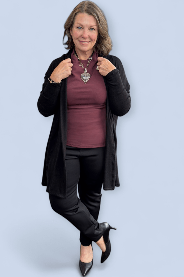 Woman wearing a black cardigan, maroon top, black pants, and black shoes on a light blue background