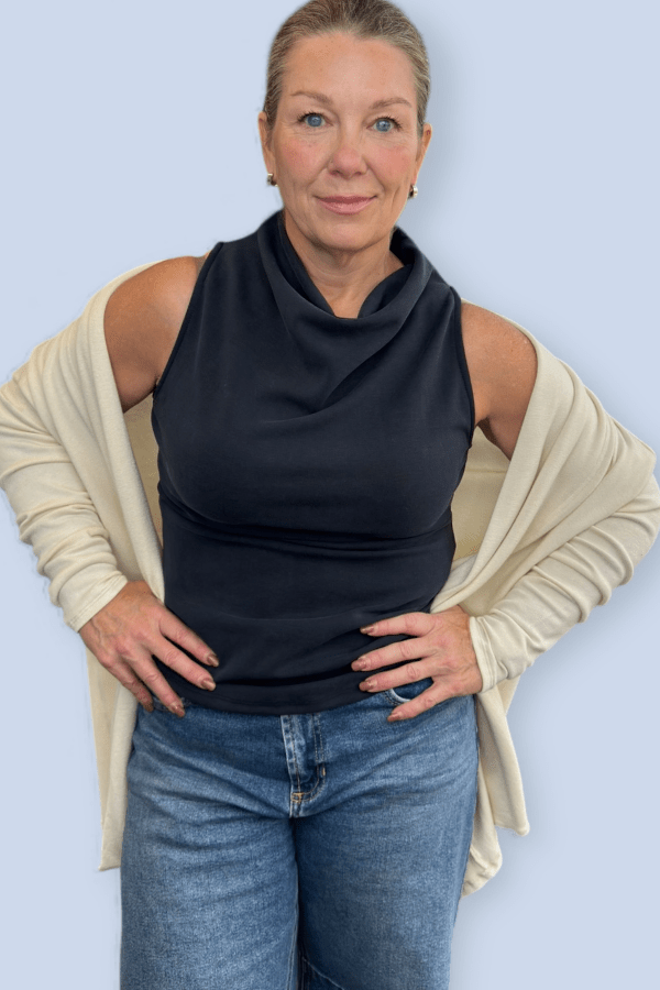 Woman wearing a black top with a cardigan over top and blue jeans.