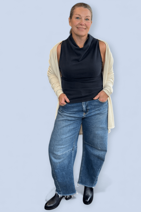 Woman wearing a black top, beige cardigan, blue jeans, and black shoes on a light blue background
