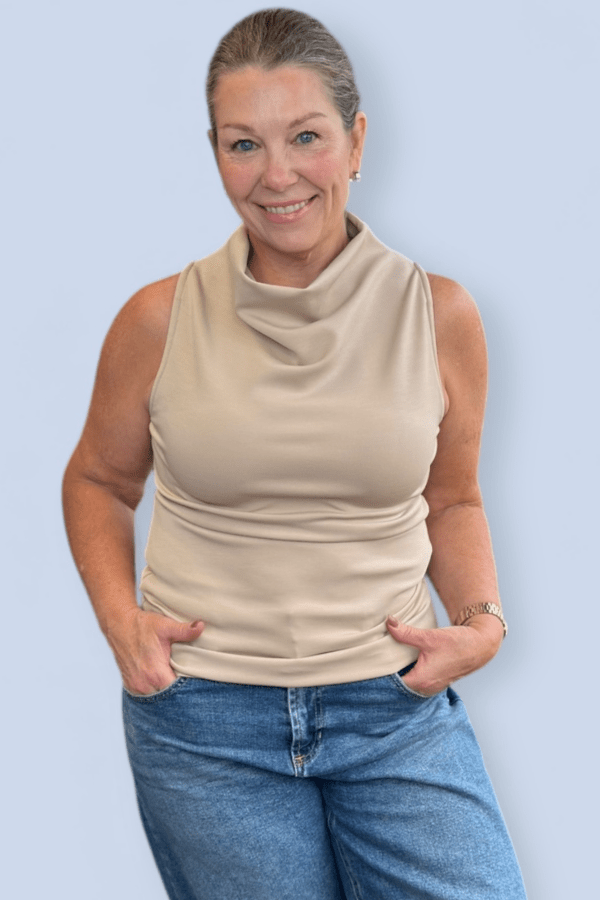 Woman wearing an ivory funnel sleeveless top.