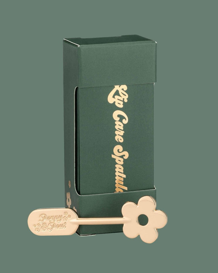 Gold Daisy Lip Spatula displayed on a green background.