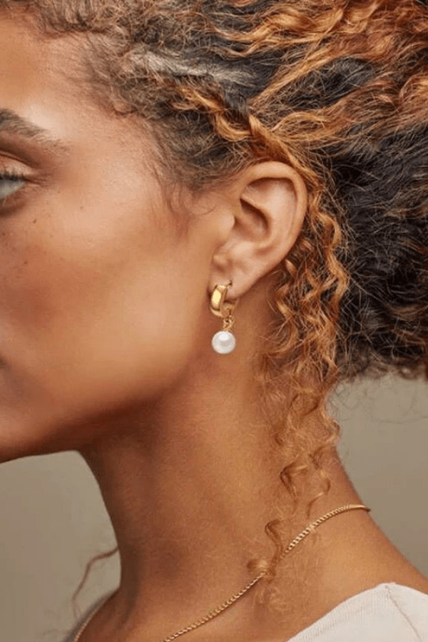 Woman wearing a gold and pearl drop earring.