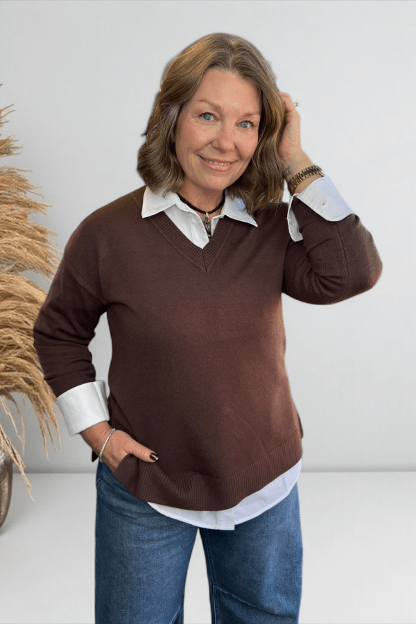 Woman wearing a brown sweater with white shirt and blue jeans against a white background