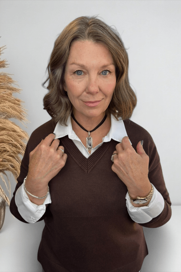 Woman wearing a brown sweater over a white shirt with a neutral background