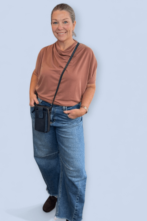 Woman wearing a rust color top with jeans and carrying a small crossbody bag.