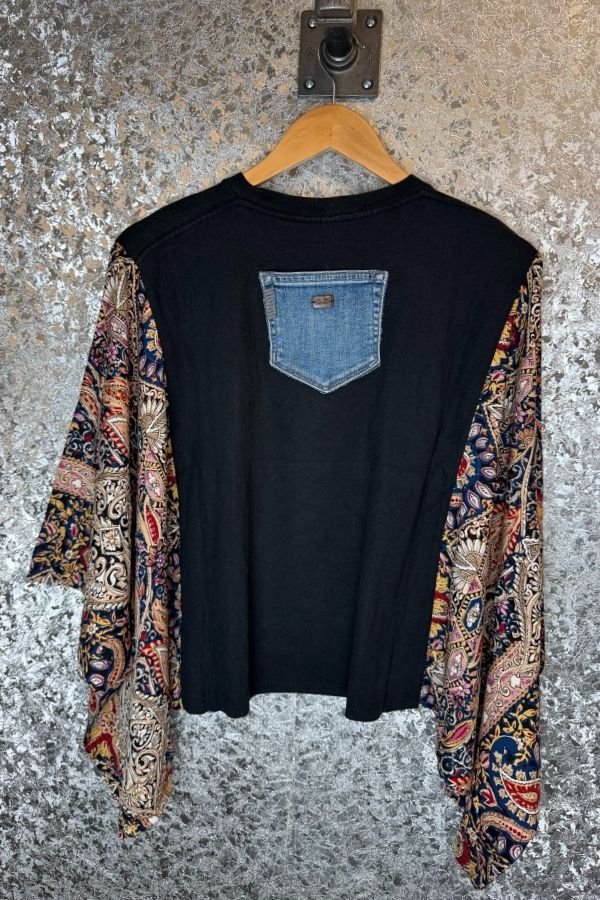 Black t-shirt with colorful sleeves on a hanger against a textured wall.