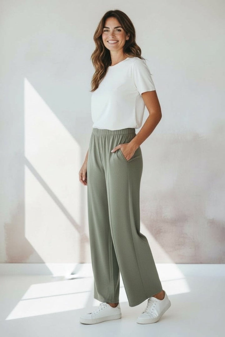 Woman wearing a white t-shirt and green pants standing in a well-lit room.