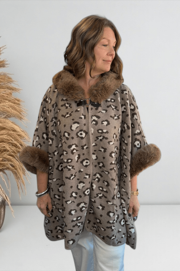 Woman wearing a leopard print poncho with fur trim against a white background