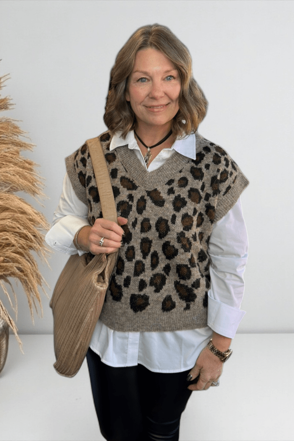 Woman wearing a leopard print vest over a white shirt, holding a beige bag.