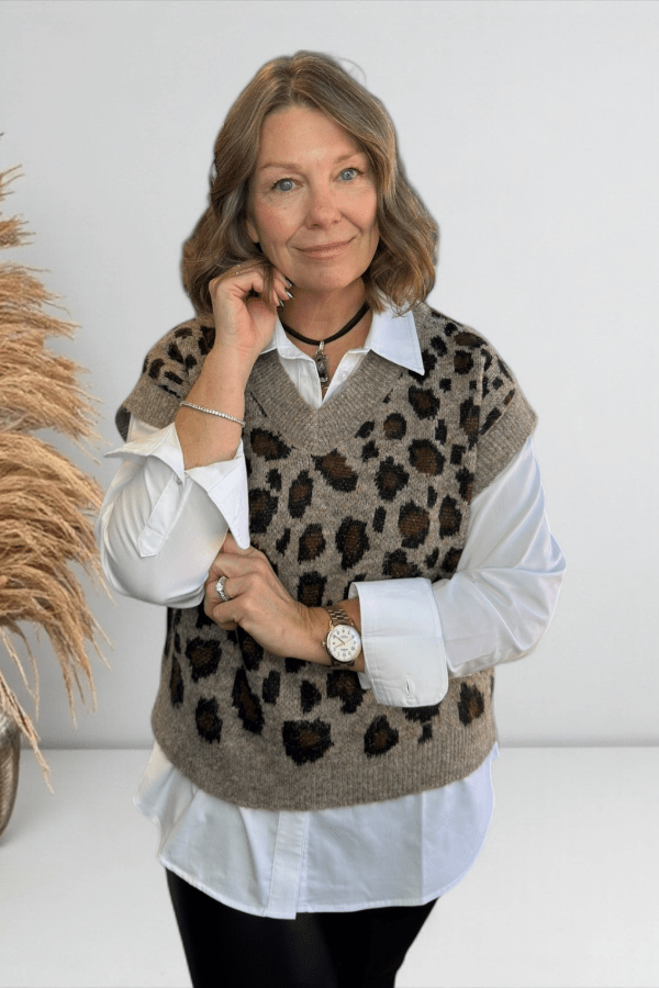Woman wearing a leopard print vest over a white shirt with a neutral background
