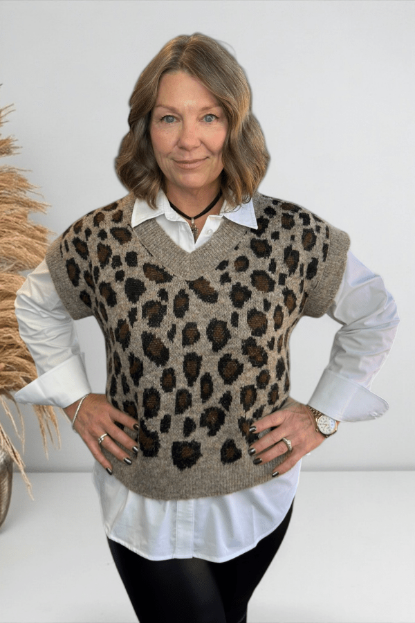 Woman wearing a leopard print vest over a white shirt with a neutral background