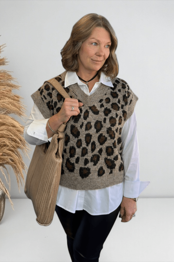 Woman wearing a leopard print vest over a white shirt, holding a beige tote bag.