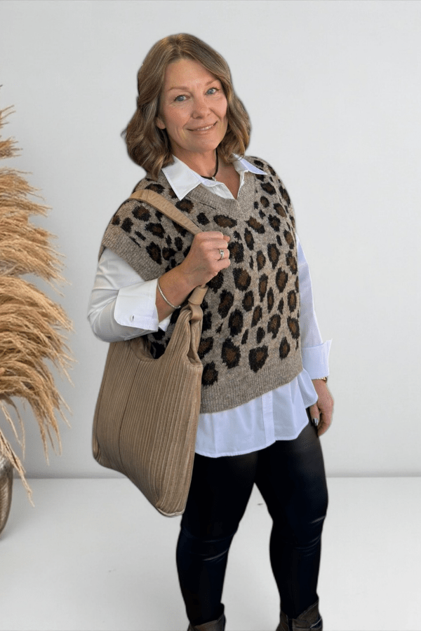 Woman wearing a leopard print vest holding a beige bag against a white background