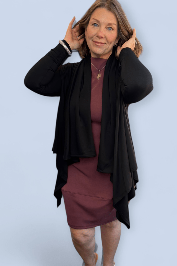 Woman wearing a black cardigan over a maroon dress against a light blue background