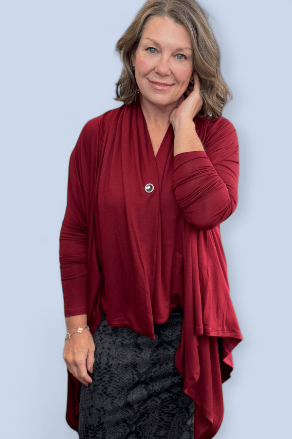 Woman wearing a red long-sleeve top with a button, standing against a light blue background.