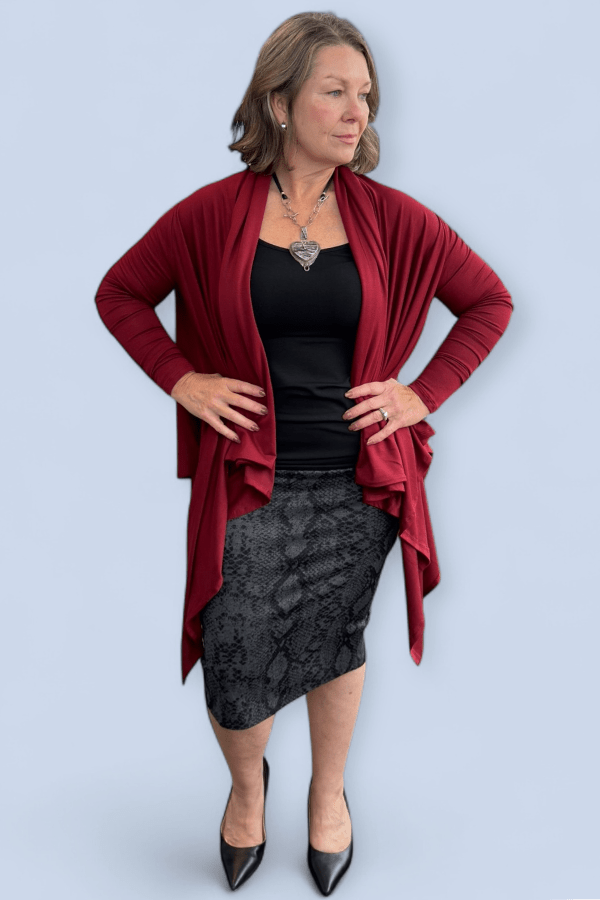 Woman wearing a red cardigan, black top, and patterned skirt on a light blue background