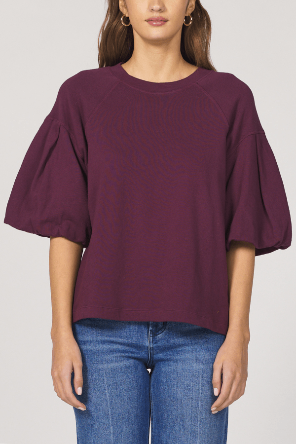 Woman wearing a purple blouse with puffed sleeves and blue jeans on a plain background