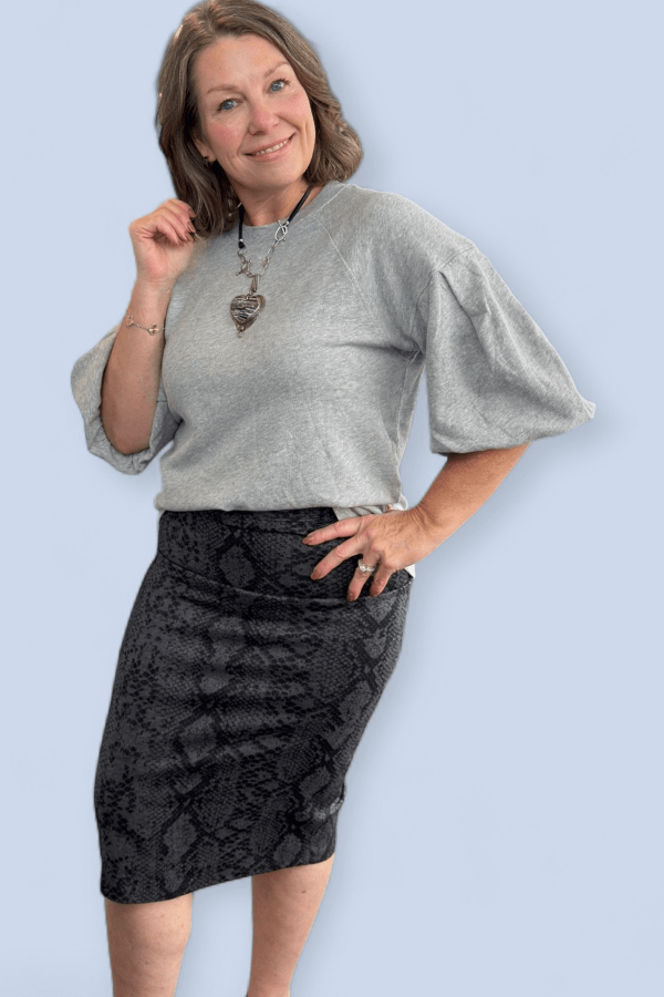 Woman wearing a gray sweater and black patterned skirt against a light blue background