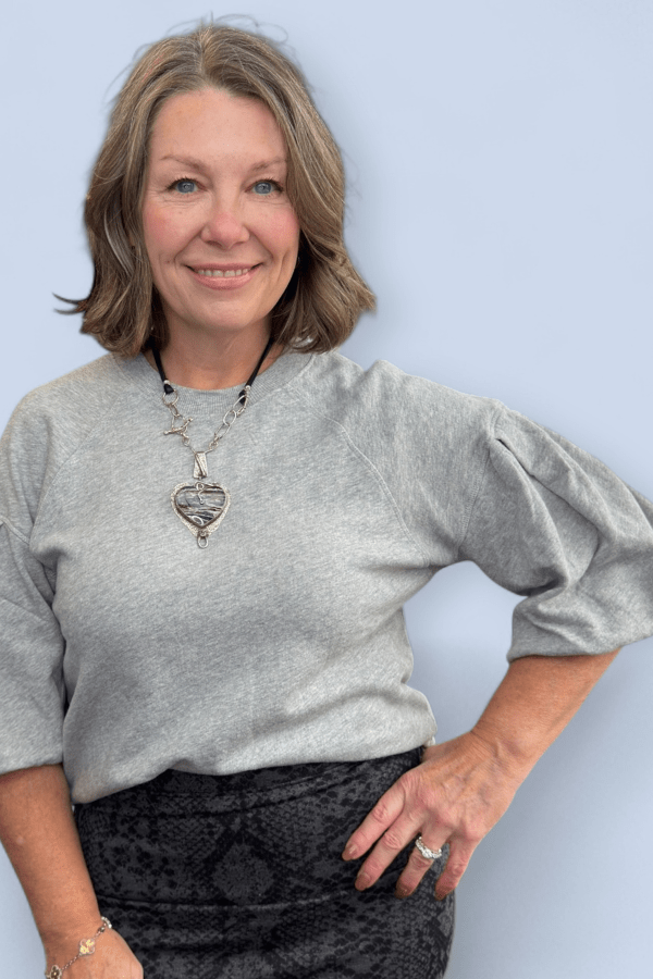 Woman wearing a gray sweater and black skirt with a plain background