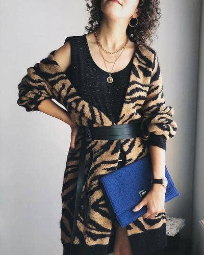 Person wearing a black and brown patterned cardigan holding a blue clutch against a neutral background