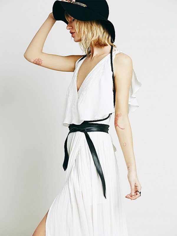 Woman wearing a white dress with a black belt and black cap on a plain background
