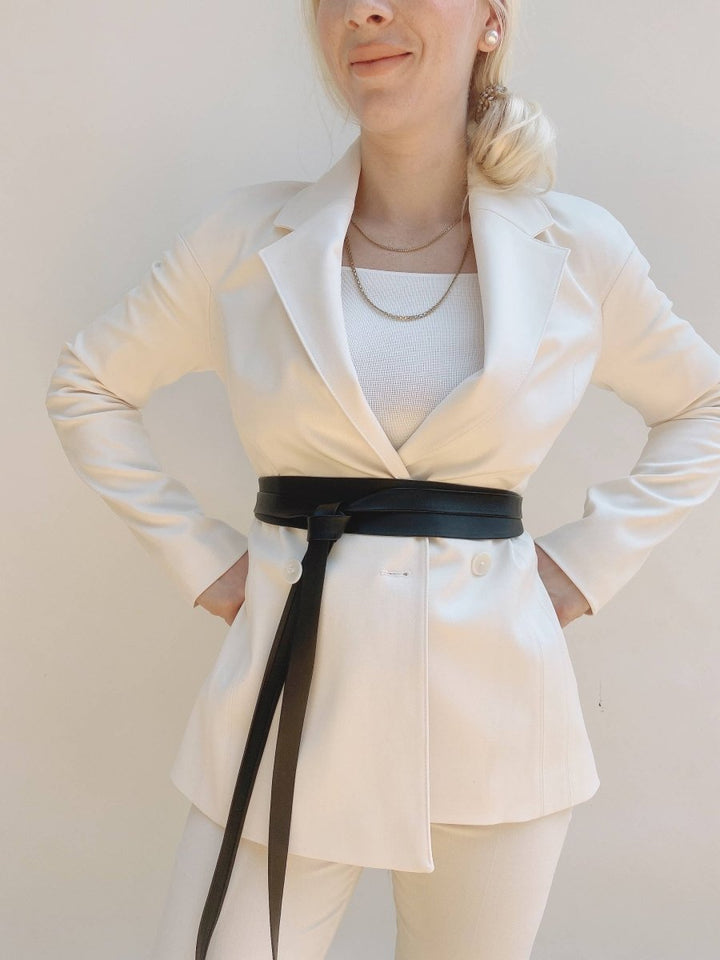 Person wearing a white blazer with a black belt against a plain background