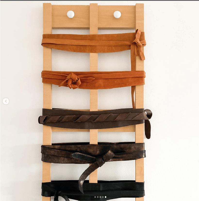 Wooden belt rack with brown, black, and tan belts on a white background