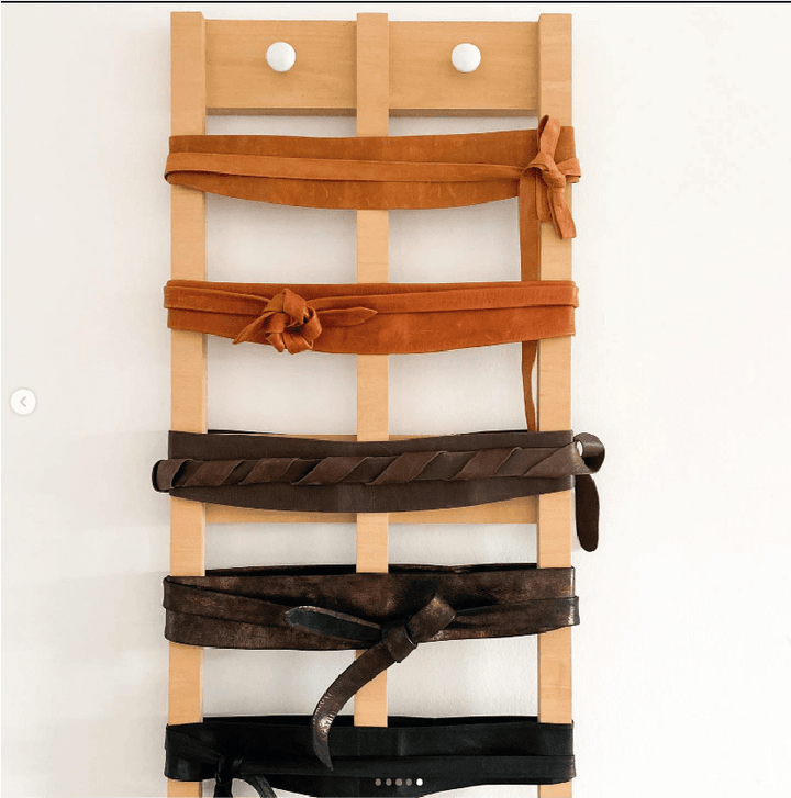 Wooden belt rack with brown, black, and tan belts on a white background