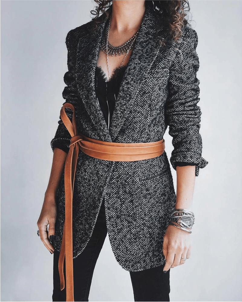 Person wearing a patterned jacket with a brown belt against a plain background