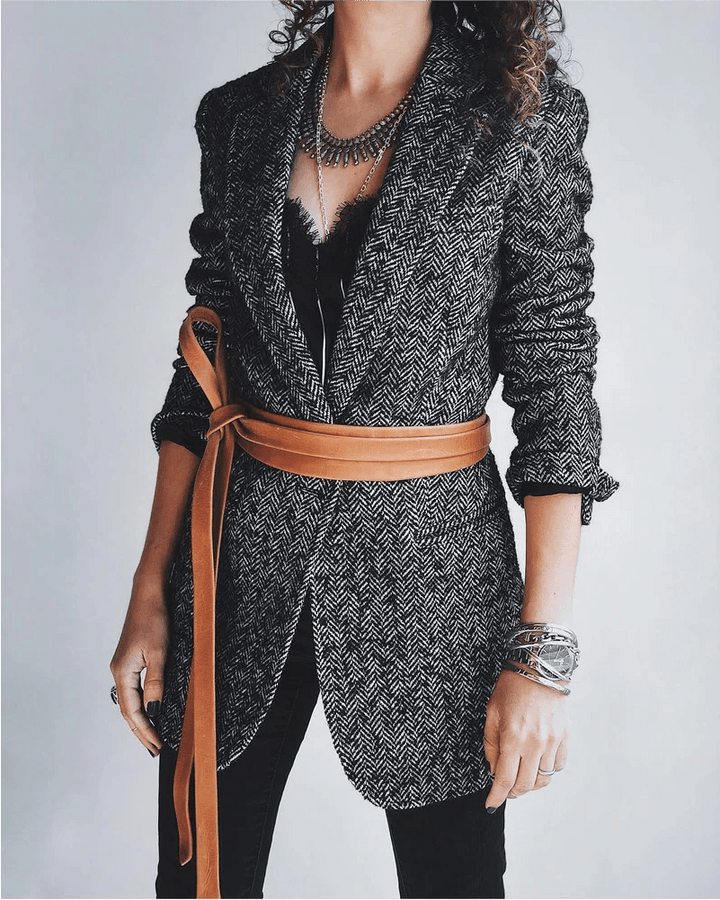 Person wearing a patterned jacket with a brown belt against a plain background