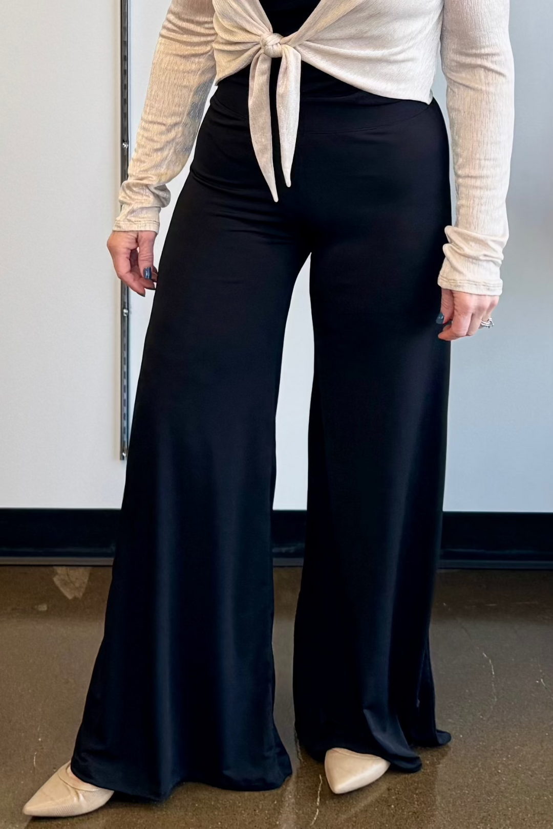 A pair of black, slim-fit knit pants with an elastic waistband, paired with a white top and beige ballet flats.