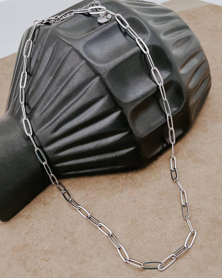 Silver chain necklace draped over a black mannequin bust on a beige surface.