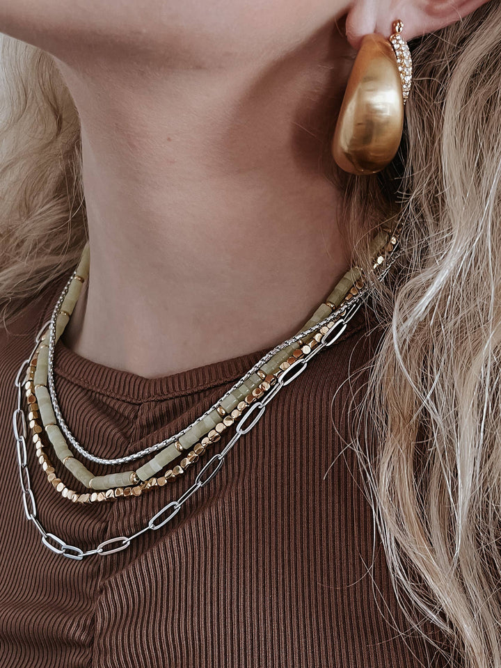 Close-up of a person wearing gold hoop earrings and layered necklaces.