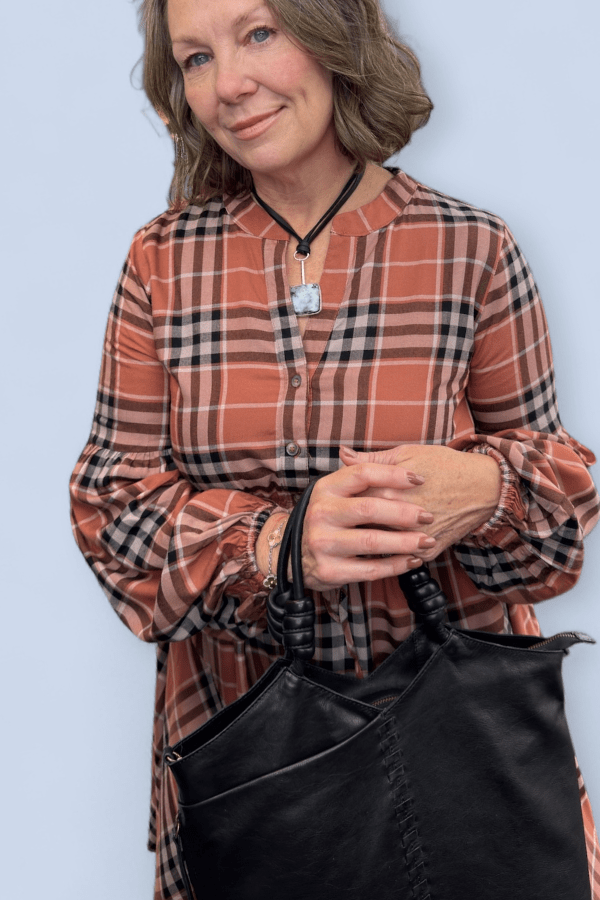 Woman wearing a plaid dress holding a black bag against a light blue background