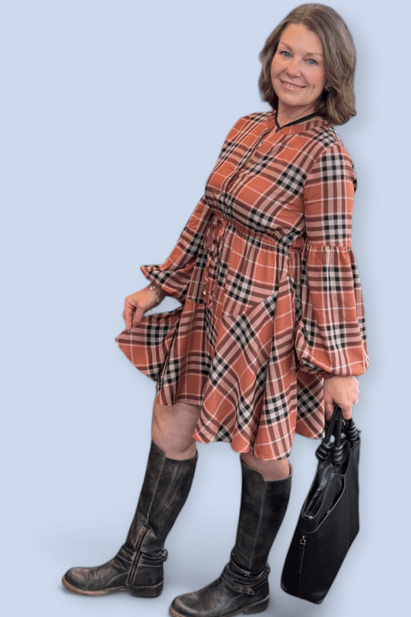 Woman wearing a plaid dress and boots holding a handbag against a light blue background