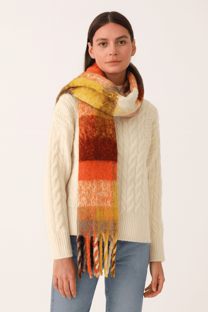 Woman wearing a plaid fringe scarf over a cream sweater with jeans.